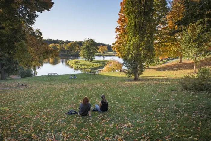 秋天，两个学生坐在天堂池塘前.